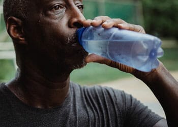A male adult gulping water from a plastic bottle
