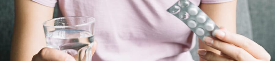 A woman holding a pill and a glass of water