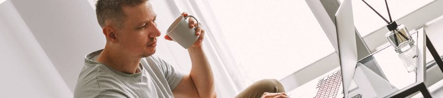 A person drinking coffee while looking at a laptop