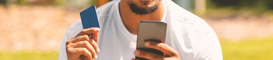 A person holding a credit card while looking at his phone outside in the park