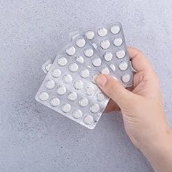 A hand holding three packs of pills