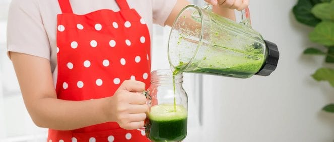 A woman pouring a detox drink in a glass from a blender