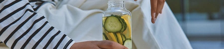 A woman holding a detox drink in a kitchen